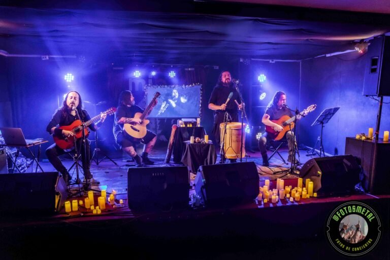 Cuatro músicos en pequeño escenario con guitarras, percusión, velas y luces azules, imagen proyectada.