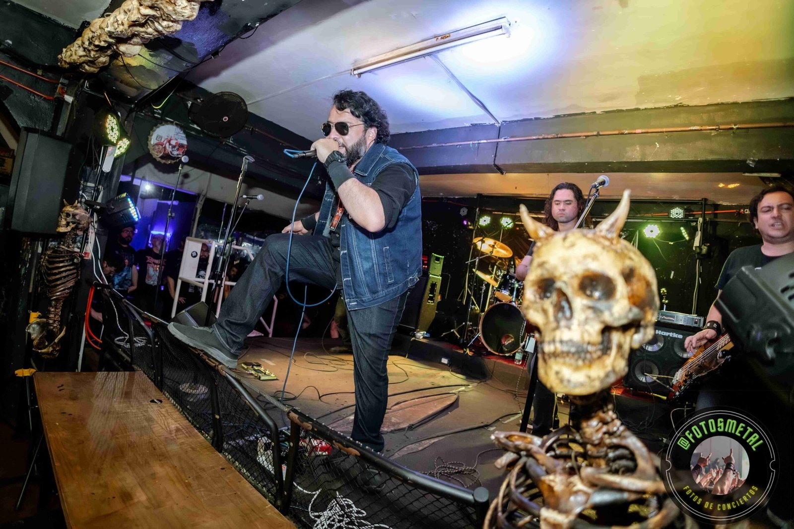 Banda de rock tocando en escenario pequeño con esqueleto decorativo con cuernos.