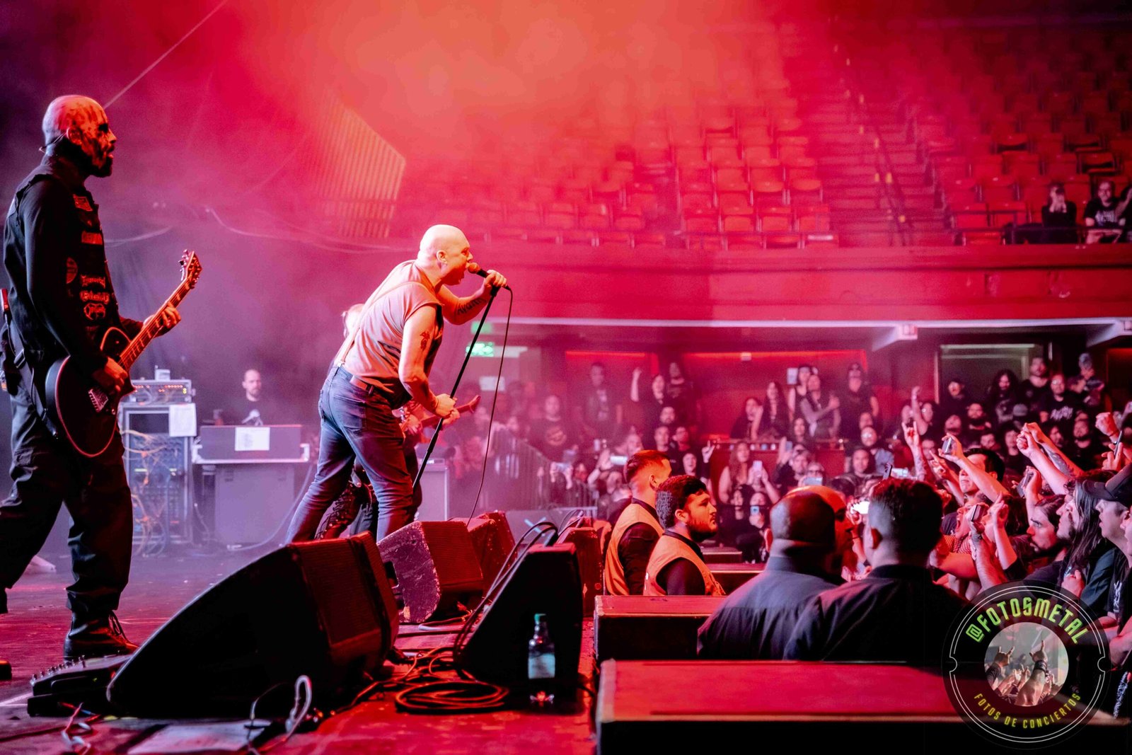 Concierto con vocalista y guitarrista en escenario, público animado y seguridad visible.