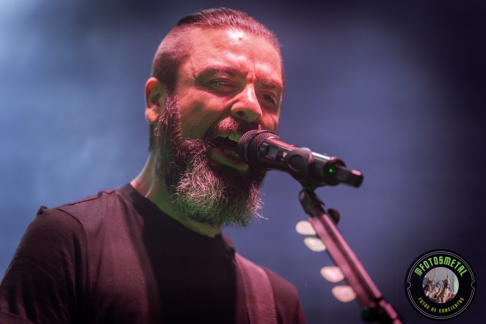 Inkoma y Pantanoscuro en Santiago: Del lodo atmosférico a la tracción directa del hard rock 1 Cantante con gafas y barba en escenario iluminado de verde apuntando y sosteniendo micrófono.
