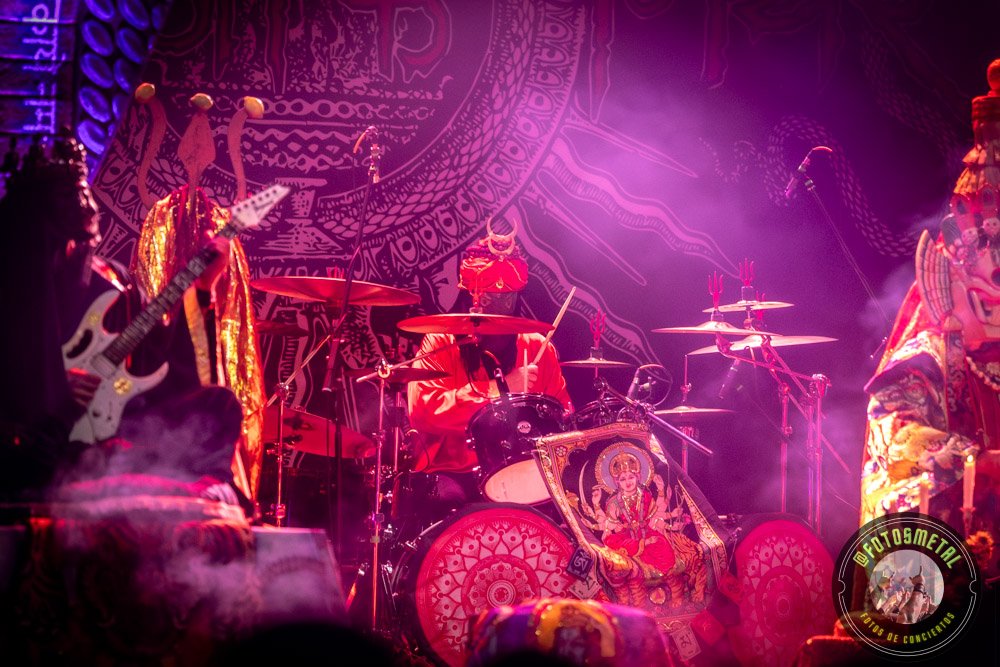 Baterista con chaqueta de cuero tocando batería en escenario iluminado durante concierto.