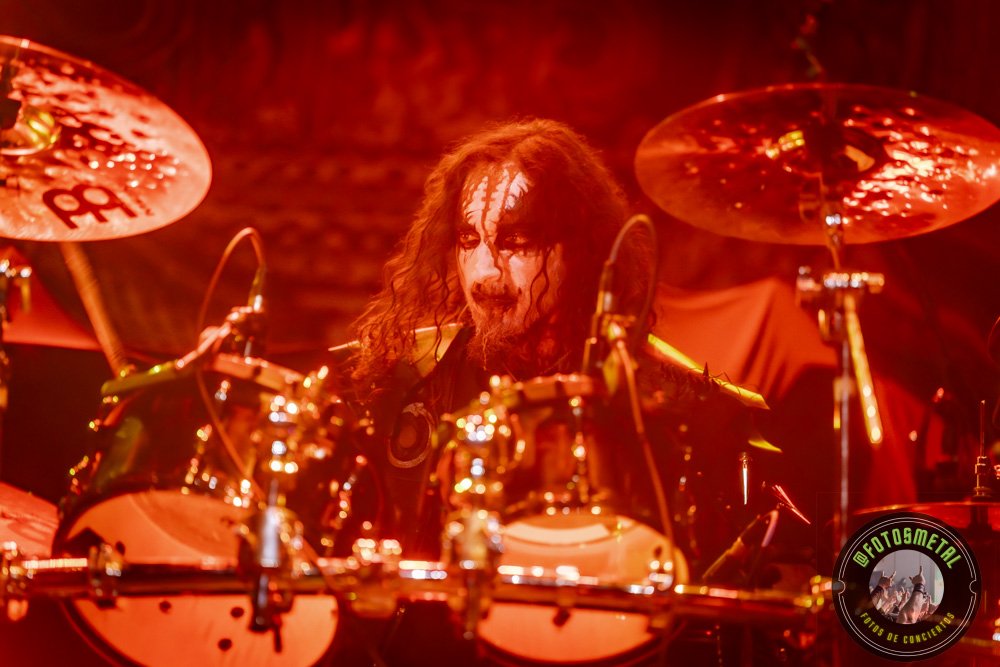 Baterista con chaqueta de cuero tocando batería en escenario iluminado durante concierto.