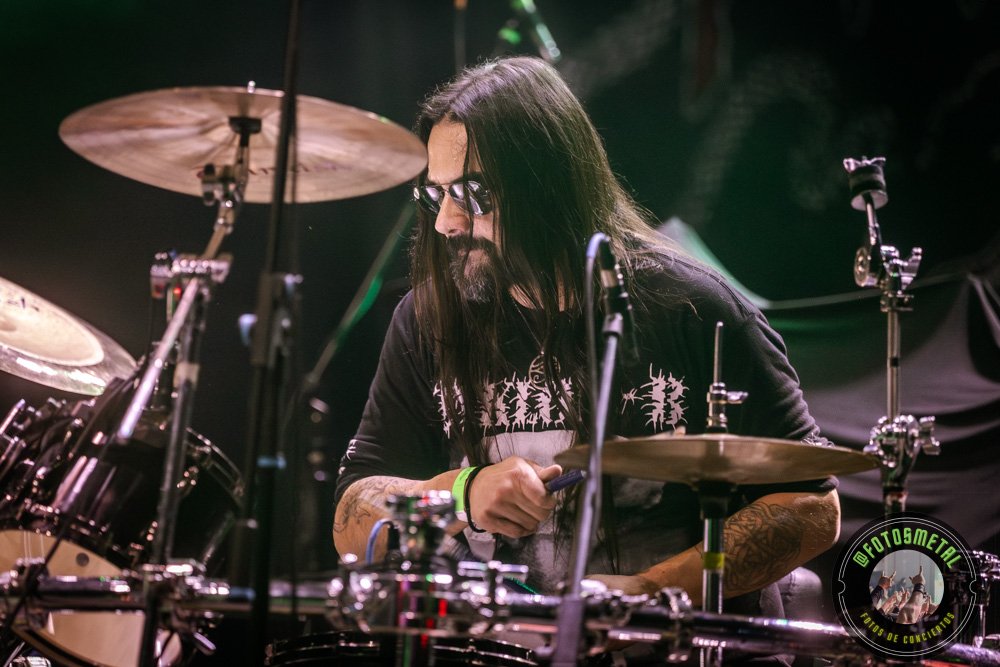 Baterista con chaqueta de cuero tocando batería en escenario iluminado durante concierto.