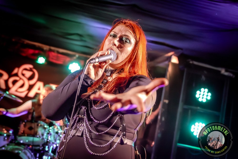 Baterista con chaqueta de cuero tocando batería en escenario iluminado durante concierto.