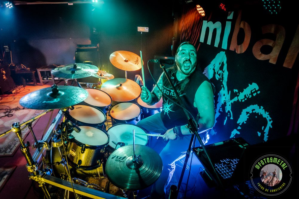 Baterista con chaqueta de cuero tocando batería en escenario iluminado durante concierto.
