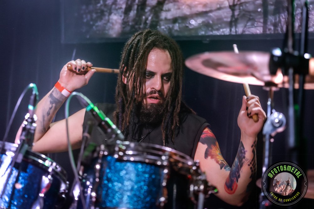 Baterista con chaqueta de cuero tocando batería en escenario iluminado durante concierto.