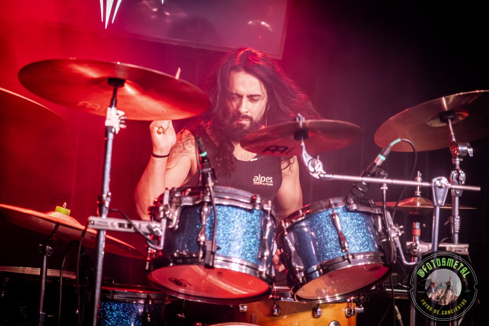 Baterista con chaqueta de cuero tocando batería en escenario iluminado durante concierto.