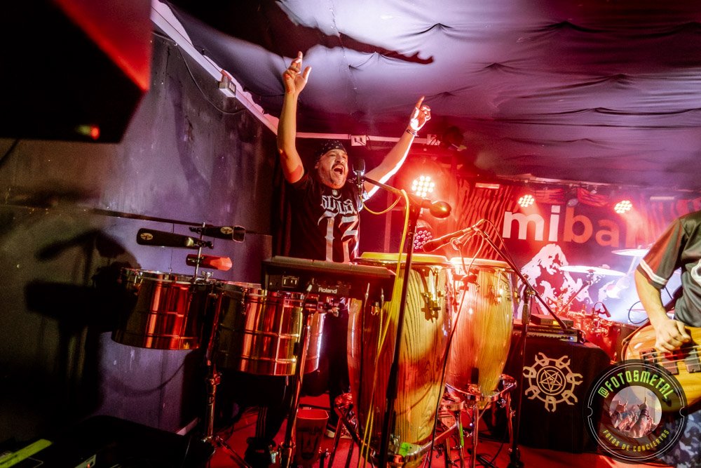 Baterista con chaqueta de cuero tocando batería en escenario iluminado durante concierto.