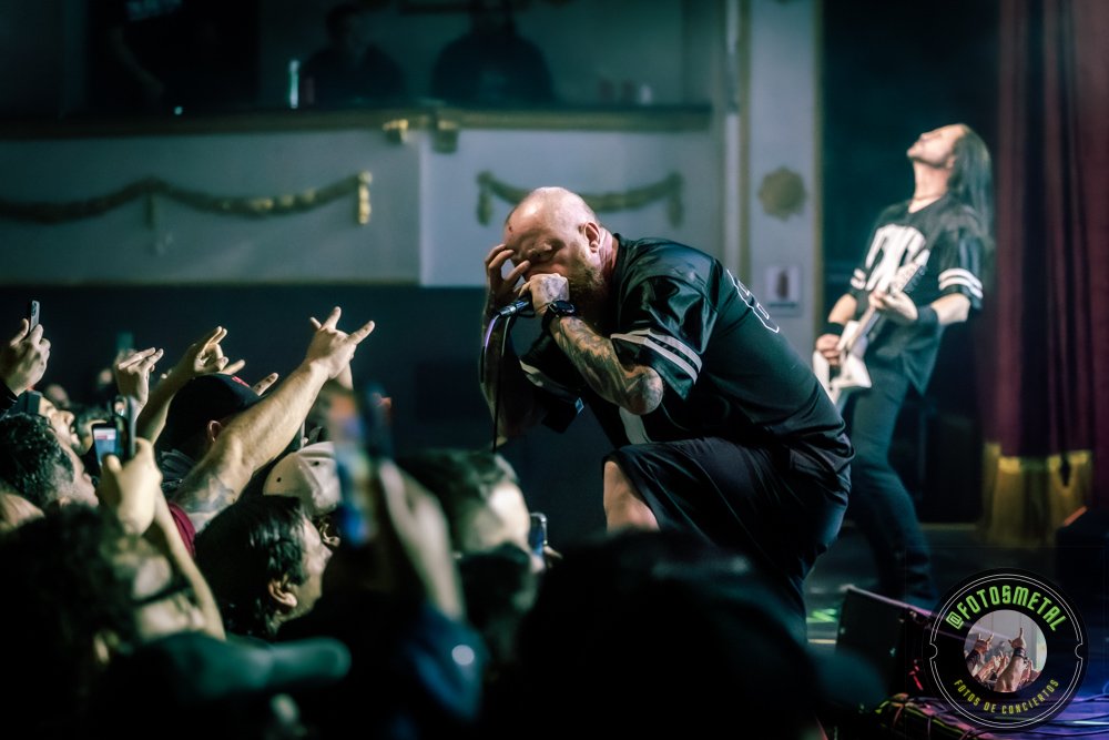 Reseña de The Haunted, Madbrain y Projector en Chile: Furia Sueca y Metal Latino 8 Primer plano del cantante con camiseta negra en escenario, micrófono y crowd levantando las manos.