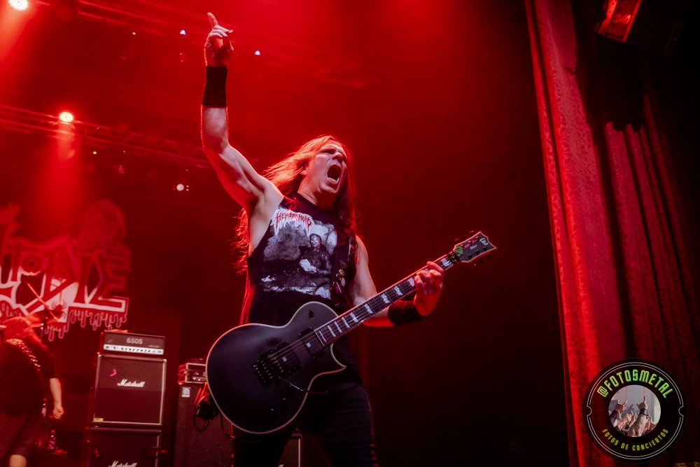 Left to Die en Chile: El eco primitivo del death metal choca en el Teatro Cariola 12 Músico de heavy metal en escenario, guitarra eléctrica negra y pulgar en alto bajo iluminación roja