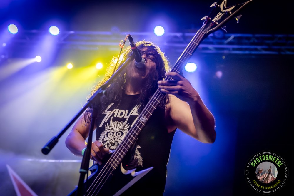 Left to Die en Chile: El eco primitivo del death metal choca en el Teatro Cariola 8 Músico con cabello largo tocando una guitarra/bajo en escenario con micrófono y luces color azul y amarillo.