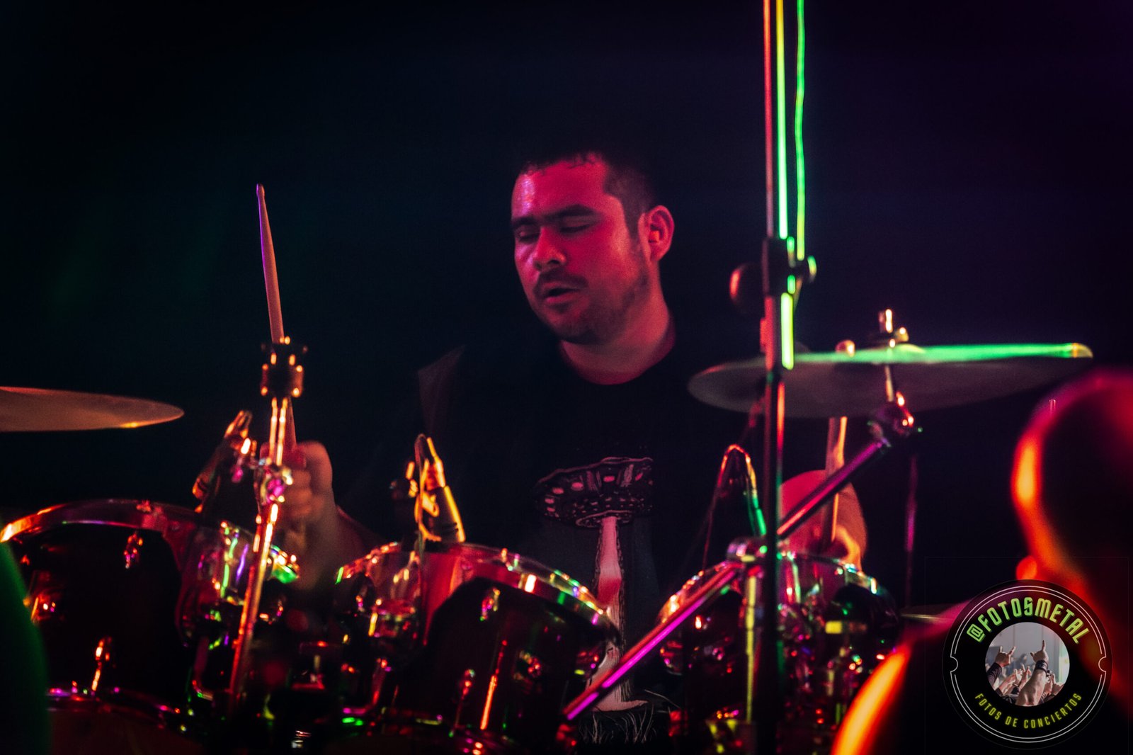 Carvakas en Metal Femfest VIII: Debut de nueva alineación en Salas FAQ Record 2 Cantante con gafas y barba en escenario iluminado de verde apuntando y sosteniendo micrófono.